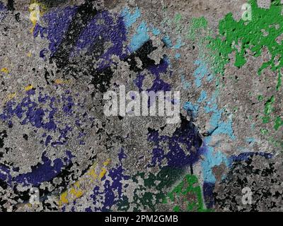 Ein altes verwittertes Graffiti-Wandgemälde mit gelben und grünen Schriftzügen schmückt einen Gehweg Stockfoto
