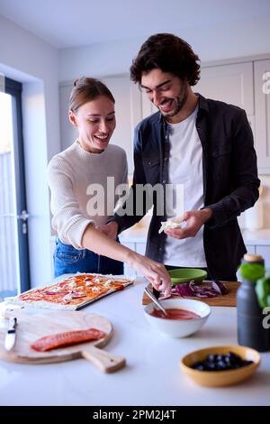 Ein Paar In Kitchen At Home, Das Zusammen Hausgemachte Pizza Macht Stockfoto