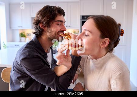 Paare In Kitchen At Home Linking Arms, Um Hausgemachte Pizza Am Tresen Zu Essen Stockfoto
