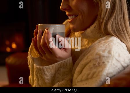 Nahaufnahme Der Frau Zu Hause In Der Lounge Mit Gemütlichem Feuer Und Heißem Getränk Stockfoto