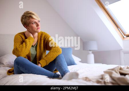 Aufmerksame Junge Frau, Die Zu Hause Im Bett Sitzt Und Aus Dem Fenster Schaut Stockfoto