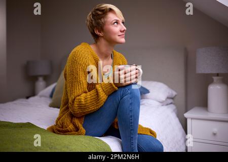 Junge Frau Mit Heißem Getränk, Die Zu Hause Im Bett Sitzt Stockfoto