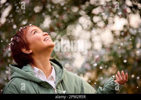Lächelnde Junge Frau Im Mantel Steht Draußen In Der Winterlandschaft Und Fängt Schneeflocken Stockfoto