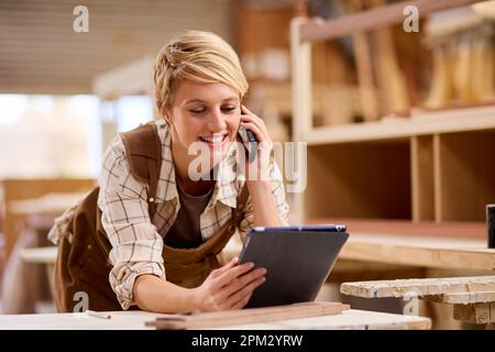 Auszubildende Mit Digitalem Tablet, Die Als Zimmerin In Der Möbelwerkstatt Telefoniert Stockfoto