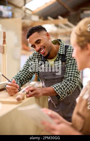 Männliche Und Weibliche Auszubildende, Die Als Zimmerleute In Der Möbelwerkstatt Arbeiten, Messen Holz Und Machen Sich Notizen Stockfoto