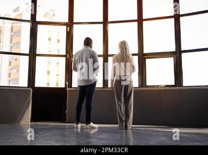 Vielseitiger Geschäftsmann Und -Frau, Die Sich In Der Nähe Von Window In Office Unterhalten Stockfoto