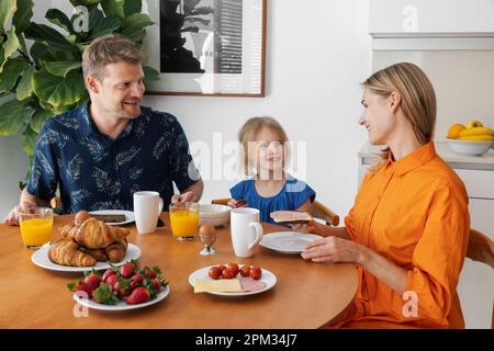 Familienfrühstück. Eltern und Kinder essen morgens am Tisch in der Küche Stockfoto