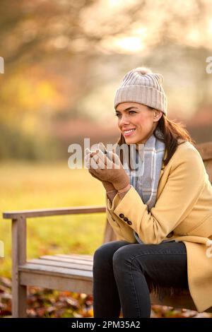 Frau Mit Hut Und Schal Mit Heißem Getränk Sitzt Auf Einer Bank Auf Einem Spaziergang In Der Herbstlandschaft Stockfoto