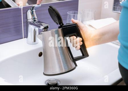 Eine Frau gießt Wasser in einen Wasserkocher in einem Hotelwaschbecken Stockfoto