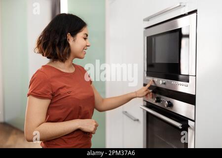 Wunderschöne arabische Frau, die in der Küche einen Elektroofen anmacht Stockfoto