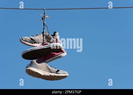 Schuhe werfen Tradition alte Schuhe, die an Drähten hängen. Turnschuhe, die an elektrischen Drähten hängen, vor einem Hintergrund mit blauem Himmel. Alte Schuhe, die an einem Draht hängen Stockfoto
