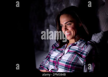 Lächelnde Frau Zu Hause, Die Nachts Im Bett Mit Einem Laptop Sitzt Stockfoto