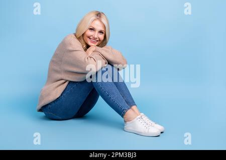 Ganzkörperprofil Porträt einer wunderschönen fröhlichen Dame Sitzboden leer und isoliert auf blauem Hintergrund Stockfoto