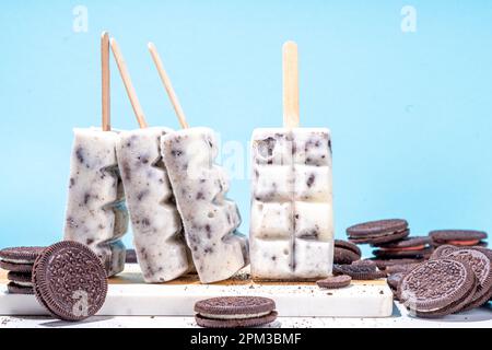 Sahne und Kekse, Eis am Stiel, Vanilleeis, Lollipops mit Schokoladen-zerdrückten Keksen, mit vielen Keksen auf dem Küchentisch hinten Stockfoto