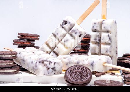 Sahne und Kekse, Eis am Stiel, Vanilleeis, Lollipops mit Schokoladen-zerdrückten Keksen, mit vielen Keksen auf dem Küchentisch hinten Stockfoto