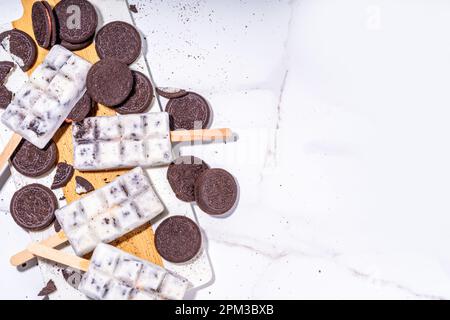 Sahne und Kekse, Eis am Stiel, Vanilleeis, Lollipops mit Schokoladen-zerdrückten Keksen, mit vielen Keksen auf dem Küchentisch hinten Stockfoto