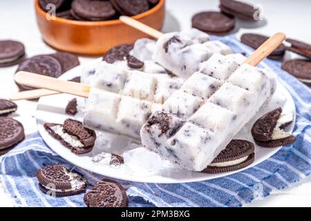 Sahne und Kekse, Eis am Stiel, Vanilleeis, Lollipops mit Schokoladen-zerdrückten Keksen, mit vielen Keksen auf dem Küchentisch hinten Stockfoto