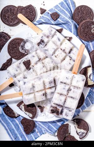 Sahne und Kekse, Eis am Stiel, Vanilleeis, Lollipops mit Schokoladen-zerdrückten Keksen, mit vielen Keksen auf dem Küchentisch hinten Stockfoto