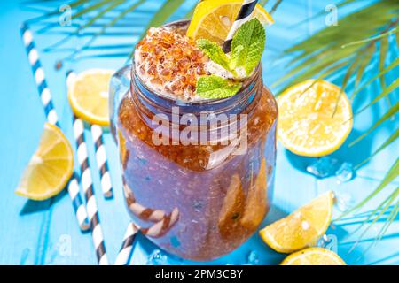 Südlicher Sweet Tea Slushy. Kalter Sommerteesüß-Dessert, hergestellt aus zerdrücktem Eistee und Zitronensaft, auf sonniger blauer Holzunterlage Stockfoto