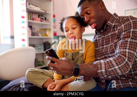 Vater und Tochter zu Hause im Mädchenschlafzimmer und posieren für Selfie am Handy und ziehen Gesichter Stockfoto