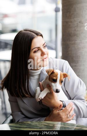 Kaukasische Frau und Jack russell Terrier schauen sich den Kuchen mit einer Kerze an. Der Hund und der Besitzer feiern den Geburtstag Stockfoto