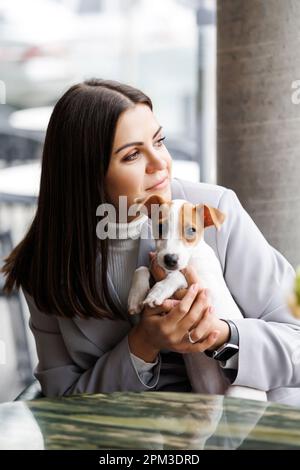 Kaukasische Frau und Jack russell Terrier schauen sich den Kuchen mit einer Kerze an. Der Hund und der Besitzer feiern den Geburtstag Stockfoto