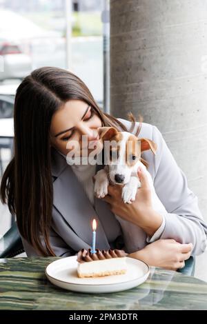 Kaukasische Frau und Jack russell Terrier schauen sich den Kuchen mit einer Kerze an. Der Hund und der Besitzer feiern den Geburtstag Stockfoto