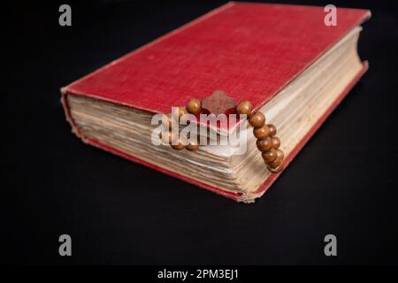 Holzperlen auf einer Schnur zwischen den Seiten eines roten, harten Einlagenbuchs auf dunklem Hintergrund. Gebetskonzept Stockfoto