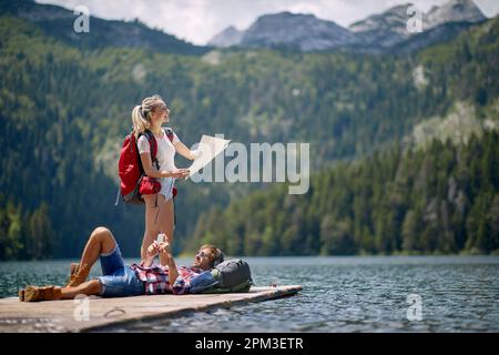 Ein junges Paar ruht sich an einem wunderschönen Tag auf dem Dock am See während einer Bergwanderung aus. Ausflug, Natur, Wandern Stockfoto