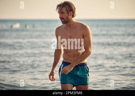 Attraktiver, sportlicher junger Erwachsener am Strand. Mann im Sommerurlaub. Urlaub, Gesundheit, aktiv, Lifestyle-Konzept. Stockfoto