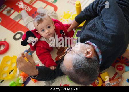 Das Baby liegt auf dem Boden und spielt mit seinem Großvater zu Hause Stockfoto