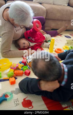 Baby spielt mit seinen Großeltern zu Hause auf dem Boden Stockfoto