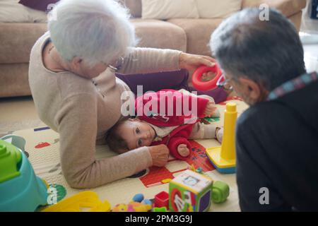 Ein kleiner Junge, der mit seinen Großeltern zu Hause auf dem Boden spielt Stockfoto