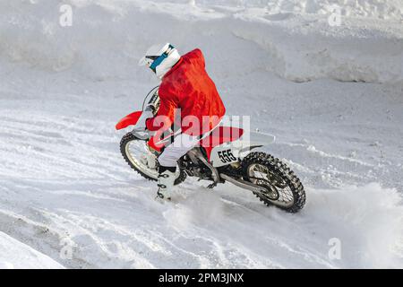 motocross-Fahrer, der im Winter Motorradrennen in scharfen Kurven fährt, Schnee spritzt unter dem Hinterrad Stockfoto