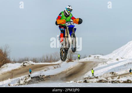 motocross-Fahrer, der auf einem verschneiten Sprungbrett springt, winterliche Off-Road-Motorradrennen Stockfoto