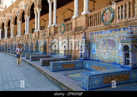 Eine Frau, die die gefliesten „Provinzalkoven“ entlang der Mauern der Plaza De Espana Sevilla Andalusien Spanien bewundert Stockfoto