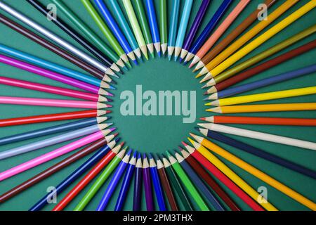 Farbstifte in Kreisform auf grünem Hintergrund. Anordnung mehrfarbiger Bleistifte. Draufsicht. Nahaufnahme. Selektiver Fokus. Stockfoto