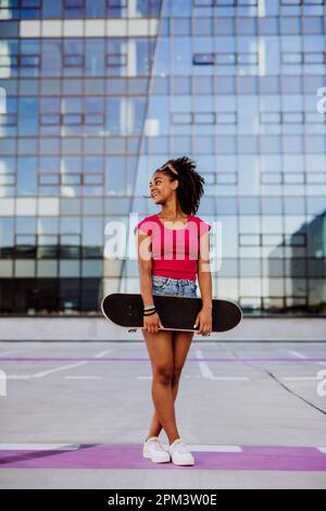 Multirassisches Teenager-Mädchen mit Rucksack und Skateboard, während des Sommers in der Stadt zu Fuß. Stockfoto