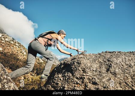 Mut wird dich weiter bringen, als du dir vorstellen kannst. Eine junge Frau, die über Felsen klettert, während sie durch die Berge wandert. Stockfoto