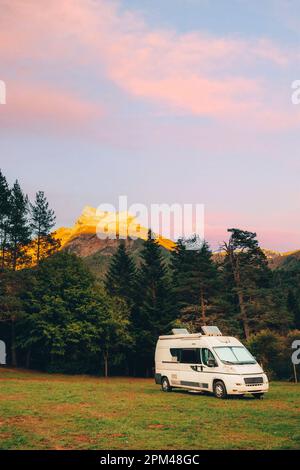 Wohnmobil in einem Camping mit herrlicher Aussicht auf den Wald und die Berge bei Sonnenuntergang. Roadtrip im Minibus und Sommerabenteuer im Freien. Nomad Stockfoto