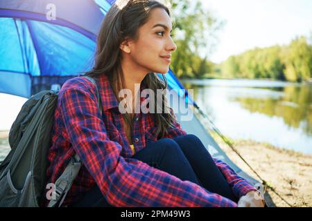 Sie entkommt allem. Eine attraktive junge Frau, die auf ihrem Campingplatz sitzt. Stockfoto