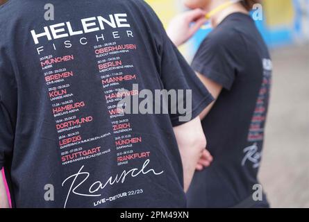 Hamburg, Deutschland. 11. April 2023. Die Fans von Helene Fischer stehen vor der Barclays Arena mit Helene Fischer T-Shirts, auf denen die Tourdaten aller Konzerte auf der Rückseite zu lesen sind. Die Sängerin Helene Fischer beginnt ihre Tour mit dem ersten von fünf Hamburger Konzerten heute Abend. Der Sänger musste den Beginn der Tour in Bremen und das Konzert in Köln aufgrund einer Rippenfraktur verschieben. Kredit: Marcus Brandt/dpa/Alamy Live News Stockfoto