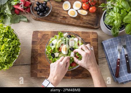Draufsicht auf weibliche Hände und Dekoration eines gesunden Frühlingssalats aus verschiedenen Zutaten. Konzept einer gesunden Lebensweise. Stockfoto