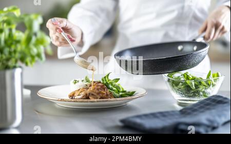 Weiblicher Koch, der das Essen mit Sauce auf der Theke im Restaurant oder in der Hotelküche zubereitet. Der Koch bereitet das Essen vor, bevor er es mit ins Restaurant nimmt. Stockfoto