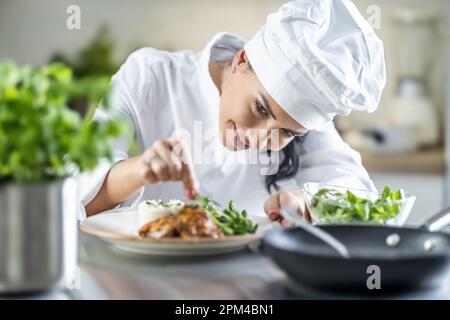 Eine junge Küchenchefin beendet das Essen mit Kräutern in der Restaurantküche. Stockfoto
