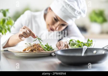 Eine junge Chefkochin beendet eine Mahlzeit mit einem Zweig Rosmarin in einer Restaurantküche. Stockfoto