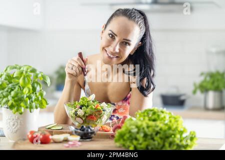 Gesunde Lebensweise junge Frau isst Salat. Junge Brünette, die in ihrer Küche gesundes Essen isst. Stockfoto