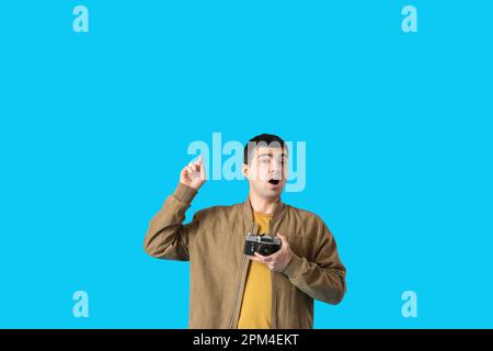 Junger männlicher Fotograf mit Retro-Kamera, die auf etwas auf blauem Hintergrund zeigt Stockfoto