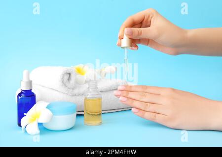 Eine Frau, die Öl auf die Nagelhaut auf farbigem Hintergrund aufträgt Stockfoto