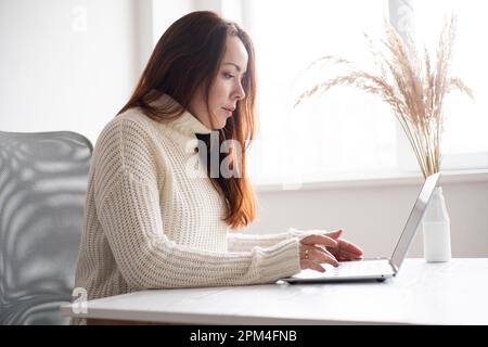 Junge Geschäftsfrau, die am Schreibtisch sitzt und online mit einem Laptop arbeitet. Mitarbeiter des Unternehmens Stockfoto